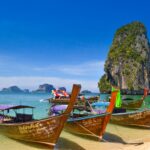 Longtail-Boote am Strand vor einem Kalksteinfelsen in Thailand