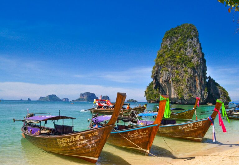 Longtail-Boote am Strand vor einem Kalksteinfelsen in Thailand